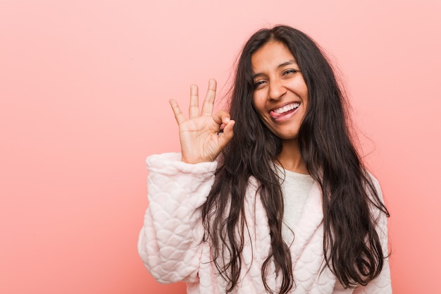 Jeune femme indienne en pyjama cligne de l'oeil et tient un geste correct avec la main