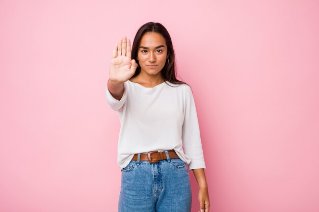 Jeune femme indienne de race mixte debout avec la main tendue montrant le panneau d'arrêt, vous empêchant.