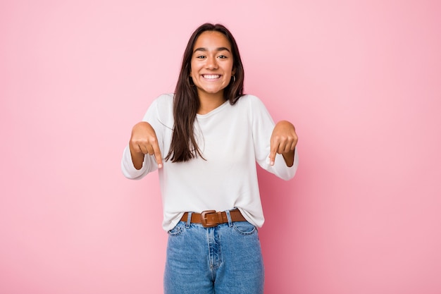 Jeune femme indienne de race mixte pointe vers le bas avec les doigts, sentiment positif.