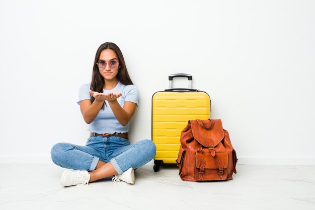 Jeune femme indienne de race mixte prête à partir en voyage tenant quelque chose avec des paumes, offrant à la caméra.