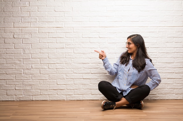 Jeune femme indienne s&#39;asseoir contre un mur de briques pointant vers le côté