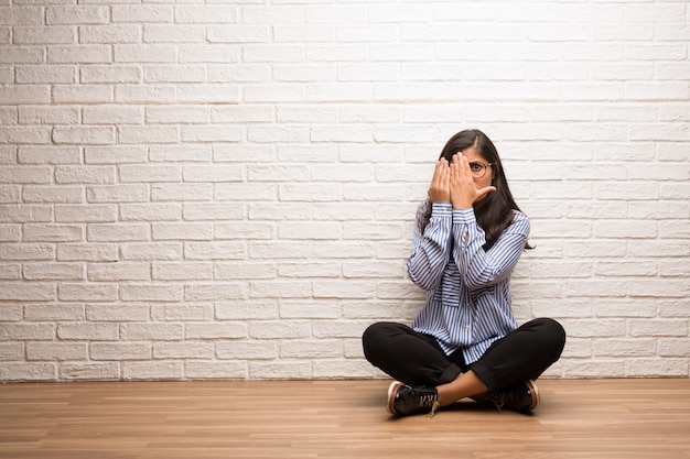 Jeune femme indienne s&#39;asseoir contre un mur de briques se sent inquiet et effrayé, regardant et couvrant