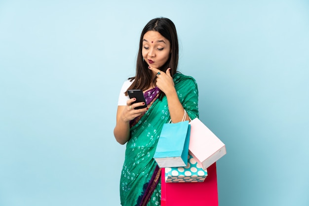 Jeune femme indienne avec des sacs à provisions en pensant et en envoyant un message