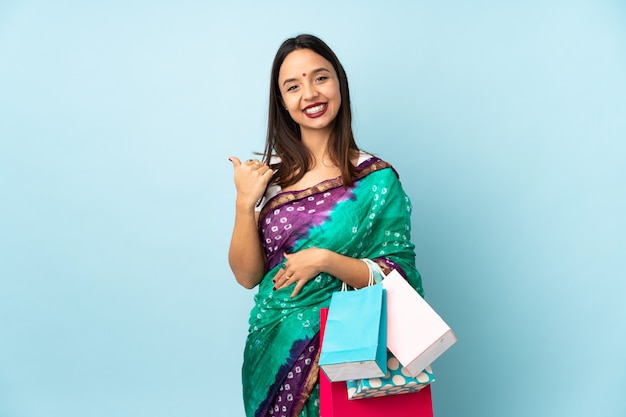 Jeune femme indienne avec des sacs à provisions pointant vers le côté pour présenter un produit