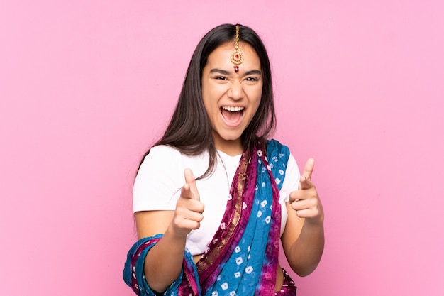 Jeune femme indienne avec sari sur mur isolé pointant vers l'avant et souriant