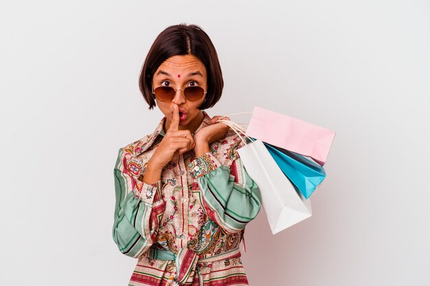 Jeune femme indienne shopping des vêtements isolés sur fond blanc gardant un secret ou demandant le silence.