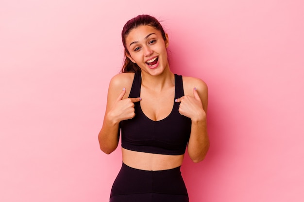 Jeune femme indienne de sport isolée sur rose surpris pointant avec le doigt, souriant largement.