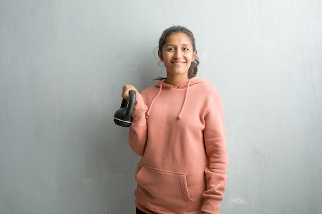 Jeune femme indienne sportive contre un mur de bonne humeur et avec un grand sourire