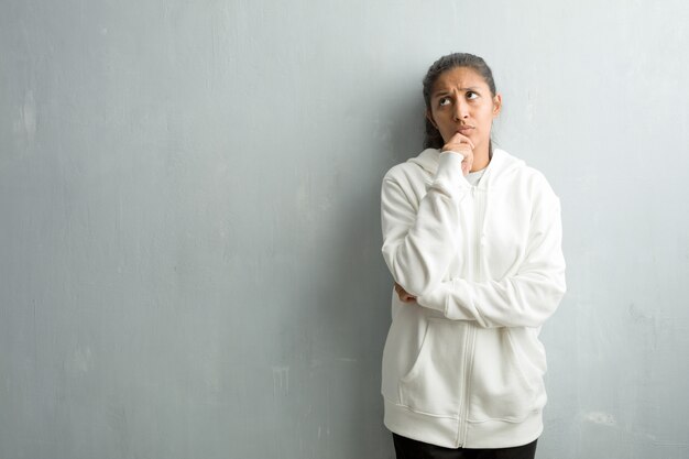 Jeune femme indienne sportive contre un mur de la salle de gym doutant et confus