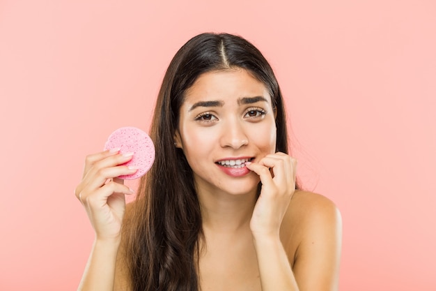 Jeune femme indienne tenant un disque de soins de la peau du visage se rongeant les ongles, nerveux et très anxieux.