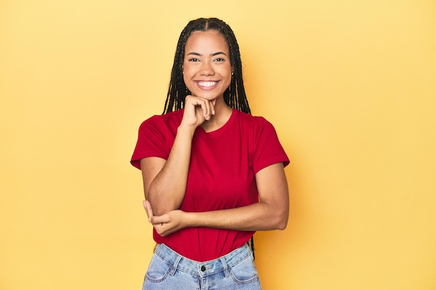 Jeune femme indonésienne sur fond jaune de studio souriant heureuse et confiante touchant le menton avec la main