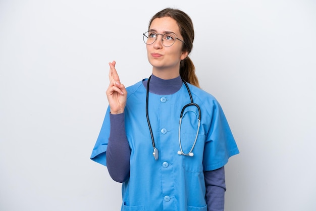 Jeune femme infirmière caucasienne isolée sur fond blanc avec les doigts croisés et souhaitant le meilleur