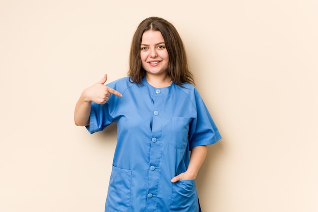 Jeune femme infirmière curvy personne pointant à la main vers un espace de copie de chemise, fier et confiant