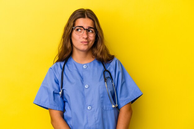 Jeune femme infirmière isolée sur fond jaune confuse, se sent dubitative et incertaine.