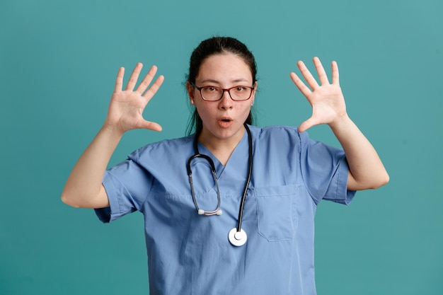 Jeune femme infirmière en uniforme médical avec stéthoscope autour du cou regardant la caméra avec sérieux montrant les paumes ouvertes numéro dix debout sur fond bleu