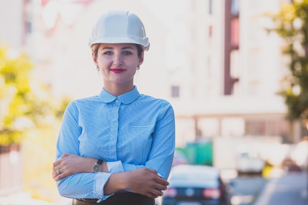 La jeune femme ingénieur dans un casque de construction blanc Elle se tient dans la ville et regarde la caméra