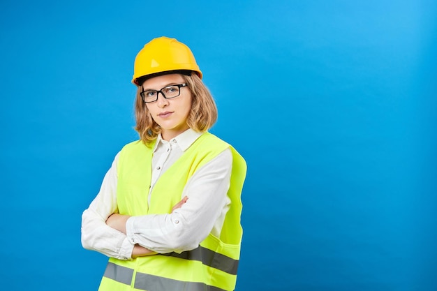 Jeune femme ingénieur portant un casque jaune debout en studio sur fond bleu Le concept de décoration de réparation de construction Prise de vue en studio