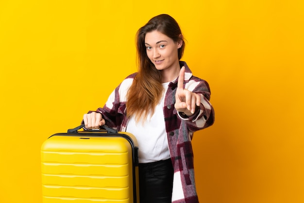 Jeune femme d'Irlande isolée sur fond jaune en vacances avec valise de voyage et en comptant un