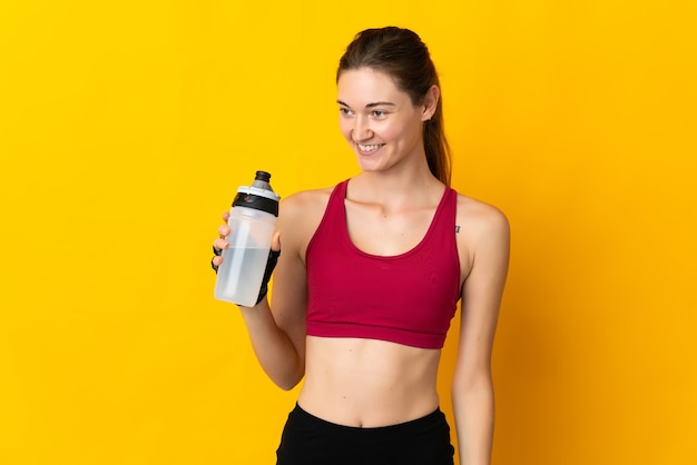 Jeune femme d'Irlande isolée sur mur jaune avec bouteille d'eau de sport