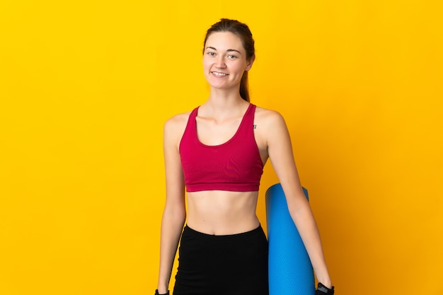 Jeune femme d'Irlande isolée sur mur jaune avec un tapis et souriant