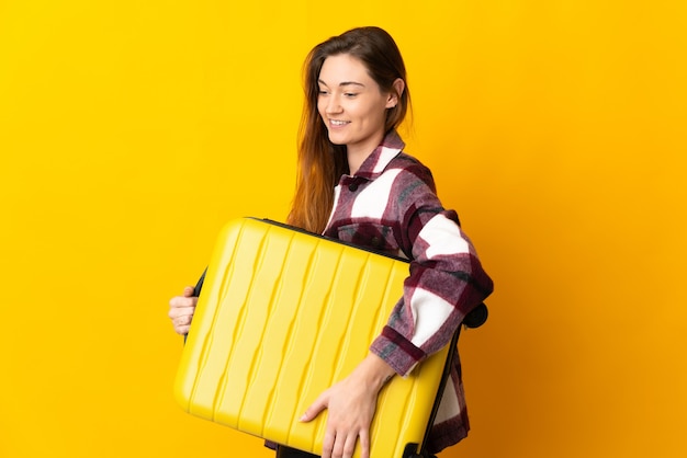 Jeune femme d'Irlande isolée sur mur jaune en vacances avec valise de voyage