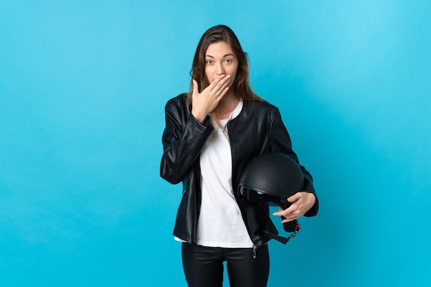 Jeune femme d'Irlande tenant un casque de moto isolé sur mur bleu heureux et souriant couvrant la bouche avec la main