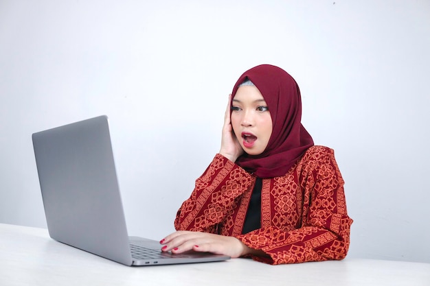 Une jeune femme islamique asiatique portant un foulard est choquée et excitée par ce qu'elle voit sur un ordinateur portable sur la table