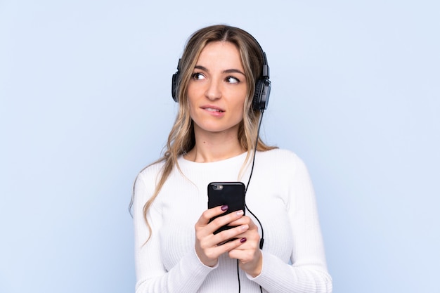 Jeune, femme, isolé, bleu, mur, écoute, musique, mobile, pensée