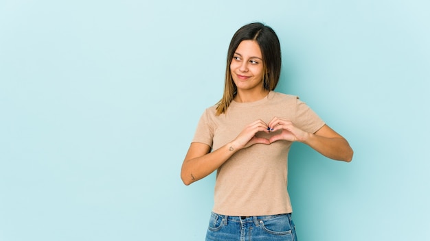 Jeune femme isolée sur bleu souriant et montrant une forme de coeur avec les mains.