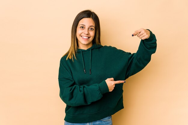 Jeune femme isolée sur fond beige tenant quelque chose de peu avec les index, souriant et confiant.