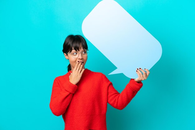 Jeune femme isolée sur fond bleu tenant une bulle vide avec une expression surprise