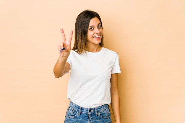 Jeune femme isolée sur un mur beige montrant le numéro deux avec les doigts.