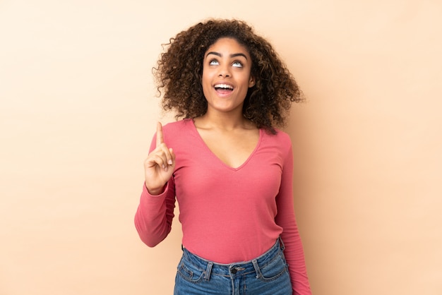 Jeune femme isolée sur un mur beige pointant vers le haut et surpris