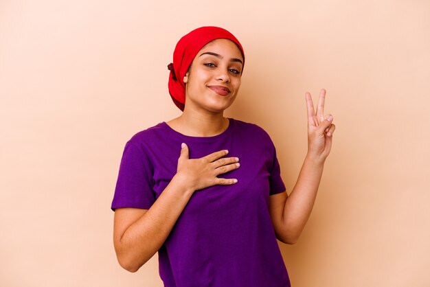 Jeune femme isolée sur un mur beige en prêtant serment, mettant la main sur la poitrine