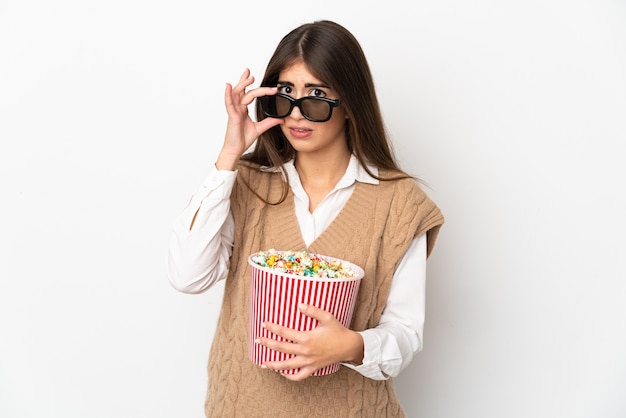 Jeune femme isolée sur un mur blanc surpris avec des lunettes 3D et tenant un grand seau de pop-corn