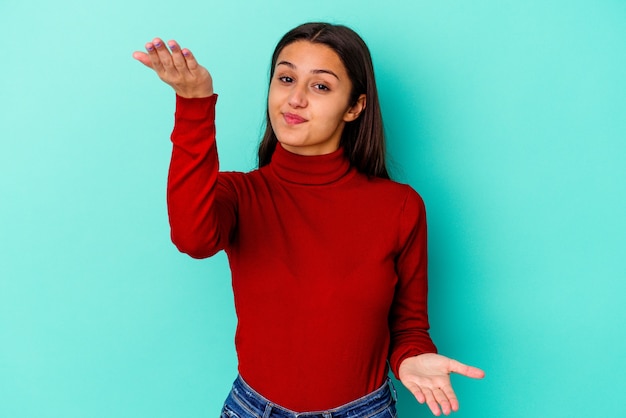 Jeune femme isolée sur un mur bleu fait échelle avec les bras, se sent heureuse et confiante