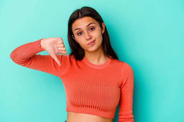 Jeune femme isolée sur un mur bleu montrant le pouce vers le bas, concept de déception