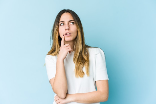 Jeune femme isolée sur un mur bleu à la recherche de côté avec une expression douteuse et sceptique