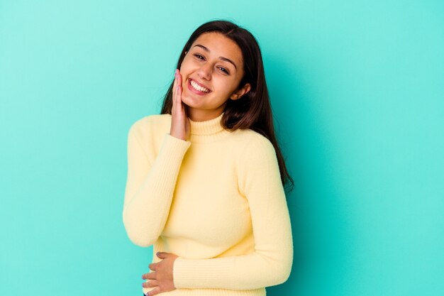 Jeune femme isolée sur le mur bleu rit joyeusement et s'amuse à garder les mains sur le ventre