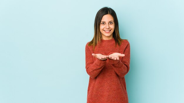 Jeune femme isolée sur un mur bleu tenant quelque chose avec des palmiers, offrant