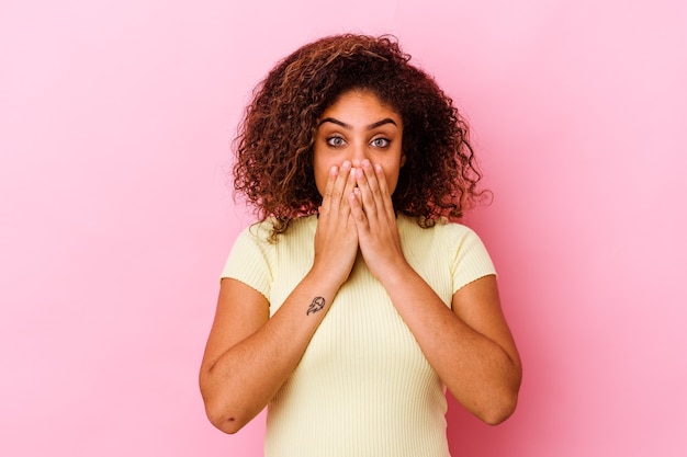 Jeune femme isolée sur un mur rose choqué, couvrant la bouche avec les mains, impatient de découvrir quelque chose de nouveau