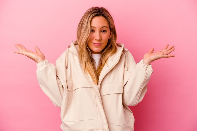 Jeune femme isolée sur un mur rose confus et douteux en haussant les épaules pour tenir un espace de copie