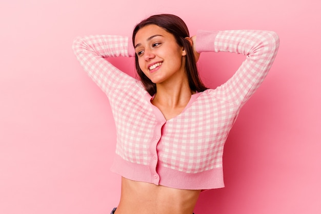 Jeune femme isolée sur un mur rose se sentir confiant, avec les mains derrière la tête