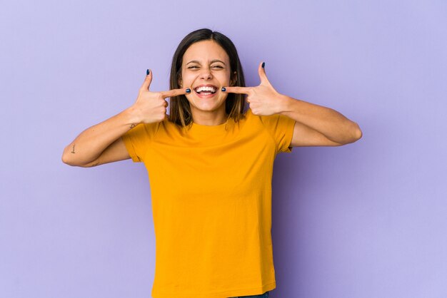 Jeune femme isolée sur le mur violet sourit, pointant du doigt la bouche.