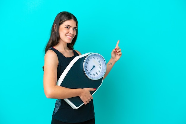 Jeune femme italienne isolée sur fond bleu avec balance et côté pointant