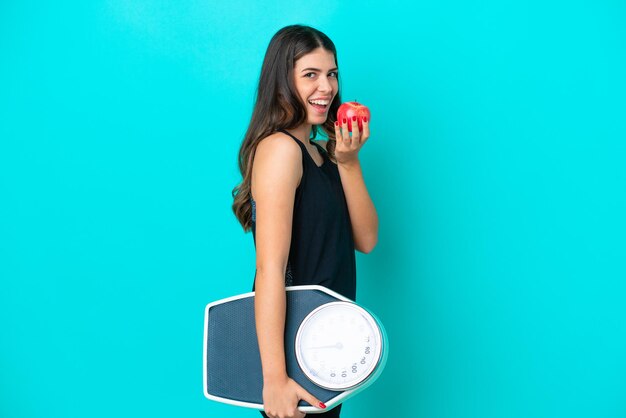 Jeune femme italienne isolée sur fond bleu avec balance et avec une pomme