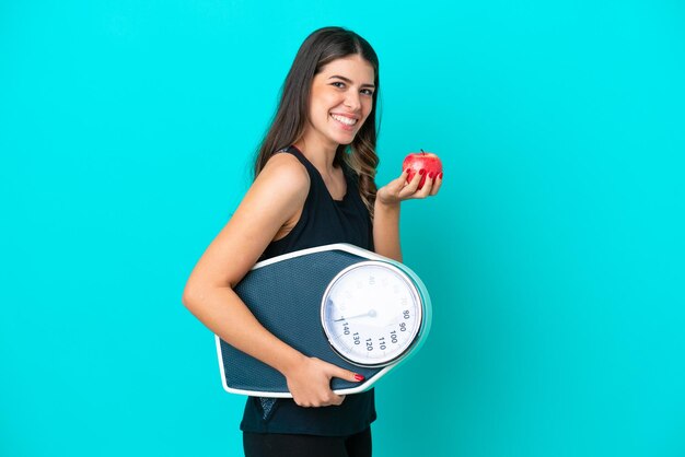 Jeune femme italienne isolée sur fond bleu avec balance et avec une pomme