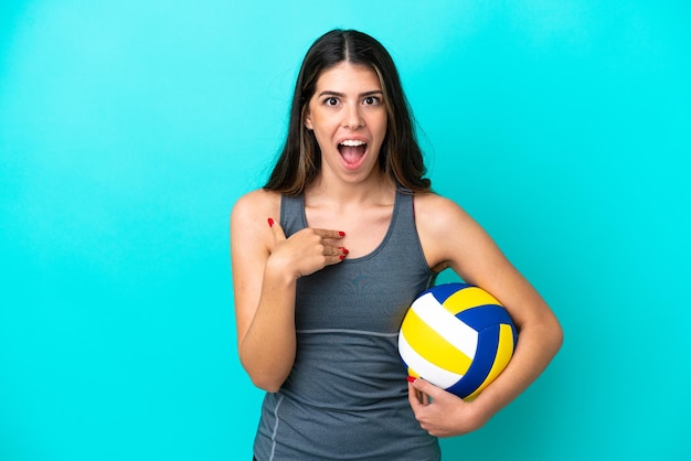 Jeune femme italienne jouant au volley-ball isolée sur fond bleu avec une expression faciale surprise