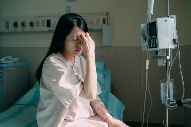 Jeune femme japonaise asiatique patiente souffrant de maux de tête avec les mains sur le front. concept médical et de soins de santé. femme malade fronçant les sourcils assise sur le lit avec une ligne IV pour garder sa santé dans la chambre d'hôpital.