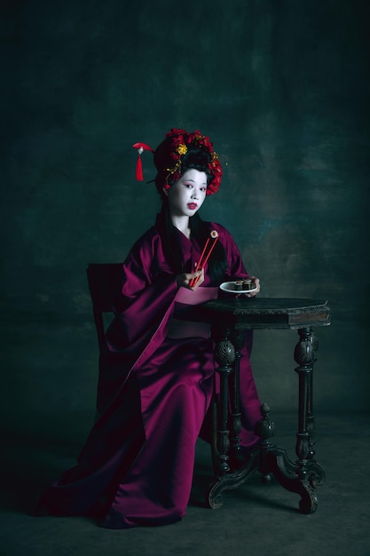 Jeune femme japonaise comme geisha sur mur vert foncé